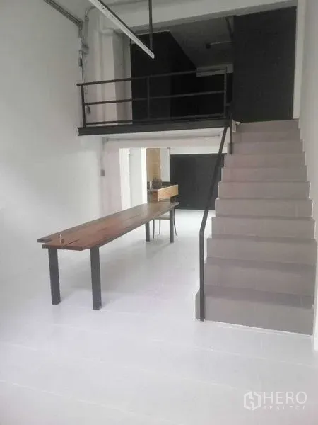 Shophouse for rent in Khlong Toei, Bangkok - Bright shophouse ground floor with mezzanine, staircase and long wooden table on white floors.