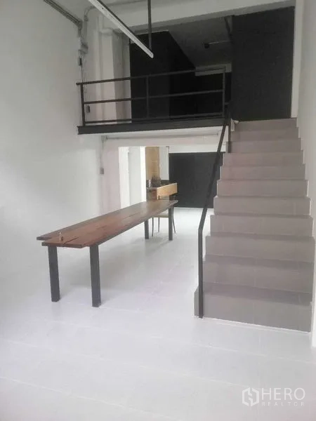 Shophouse for rent in Khlong Toei, Bangkok - Bright shophouse ground floor with mezzanine, staircase and long wooden table on white floors.