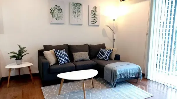 Condominium for rent in Phra Khanong, Bangkok - Bright living room with gray sectional sofa, modern coffee table, floor lamp, botanical wall art and wood flooring.