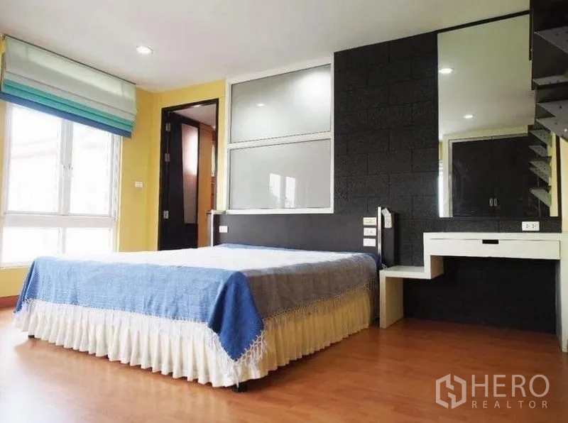 Townhouse for rent in Wang Thonglang, Bangkok - Bright bedroom with large window, black accent wall, vanity desk and wood flooring.
