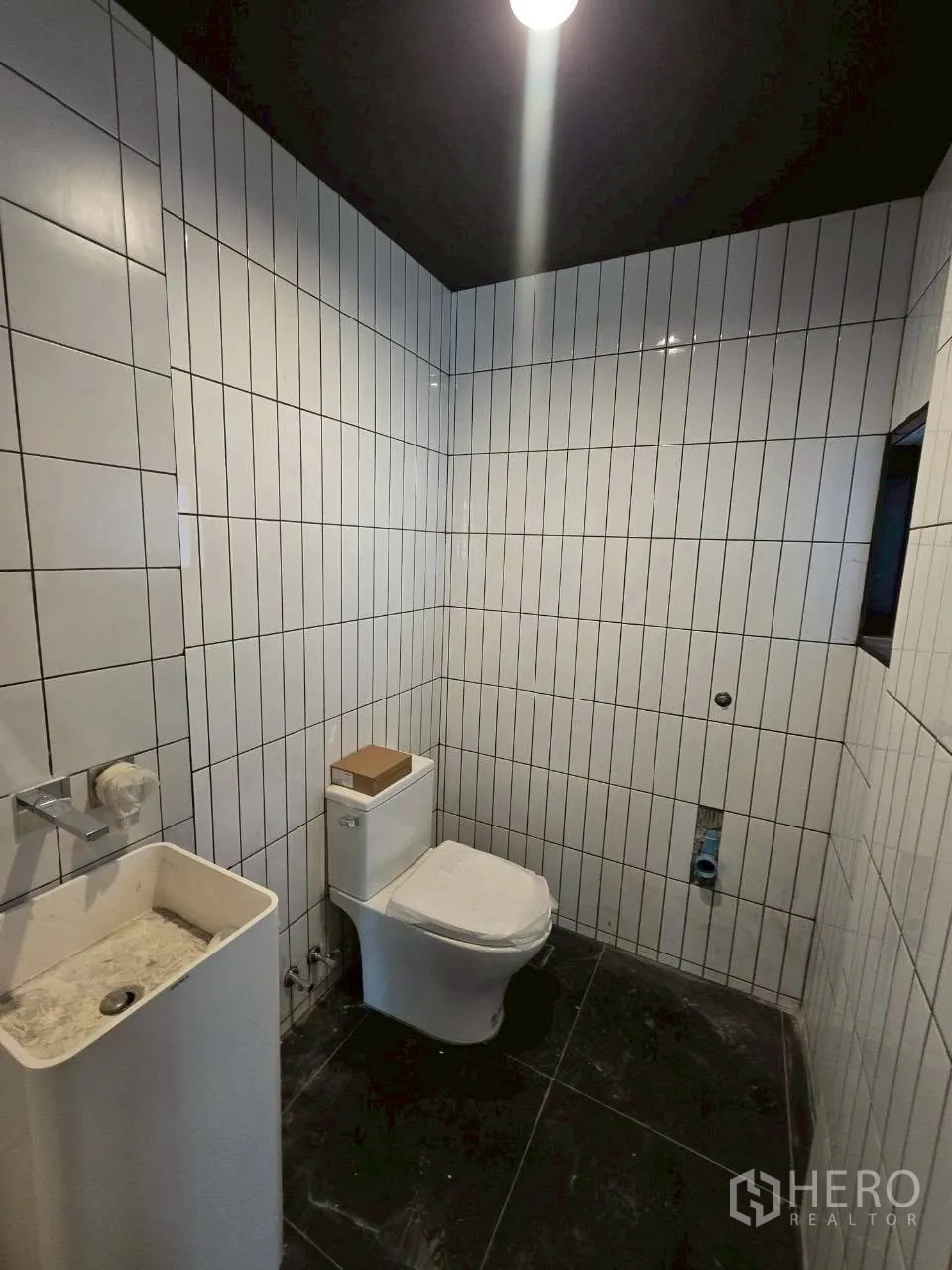 Detached House for rent in Phra Khanong, Bangkok - Bathroom with vertical white tiles, toilet, and pedestal sink under a dark ceiling.