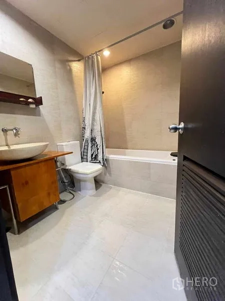 Condominium for rent in Ratchathewi, Bangkok - Modern bathroom with bathtub, vessel sink vanity, and neutral wall tiles.