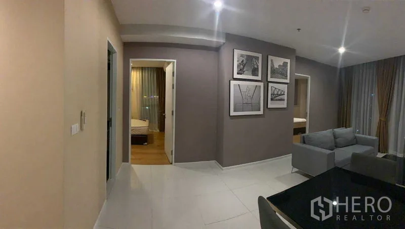 คอนโด ให้เช่าในWatthana, Bangkok - โถงทางเดินไปยังสองห้องนอน ผนังประดับกรอบภาพ พื้นกระเบื้องเงา และพื้นที่นั่งเล่นสว่างด้วยหน้าต่างบานใหญ่