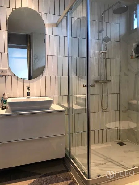 Townhouse for rent or sale in Khlong Toei, Bangkok - Second bathroom with walk‑in glass shower, vanity and vertical white tiles.