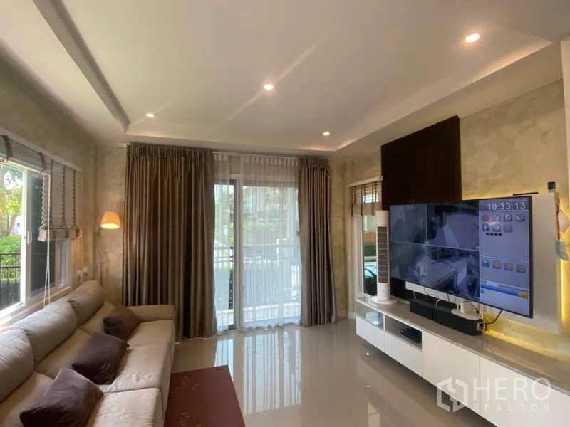 บ้าน ขายในBang Sao Thong, Samut Prakan - ห้องนั่งเล่นสว่างด้วยหน้าต่างบานใหญ่ ไฟดาวน์ไลท์ และชั้นวางทีวี