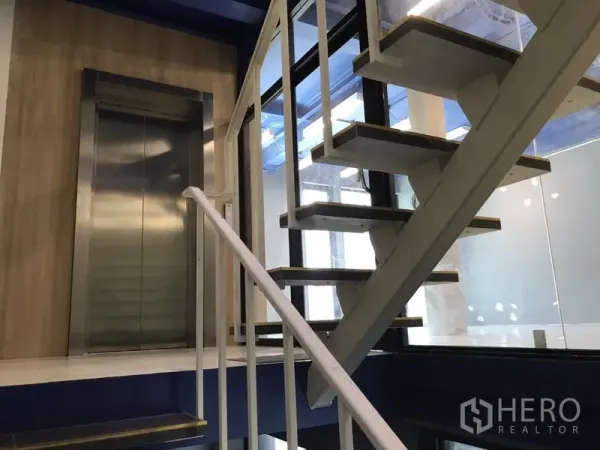 Office Space for rent in Watthana, Bangkok - Modern internal staircase beside a stainless-steel elevator with floor-to-ceiling glass in a Phra Khanong office.