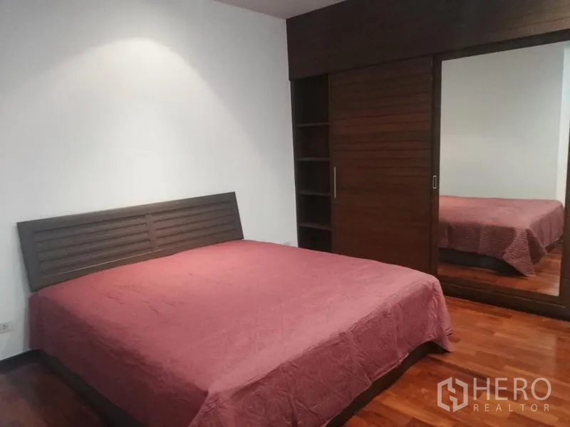 Condominium for rent in Watthana, Bangkok - Spacious bedroom with king bed, wood floors and a mirrored built-in wardrobe.