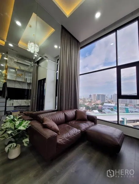 คอนโด ให้เช่าในChatuchak, Bangkok - โซฟาหนังสีน้ำตาลข้างหน้าต่างพาโนรามา มองเห็นสกายไลน์กรุงเทพฯ