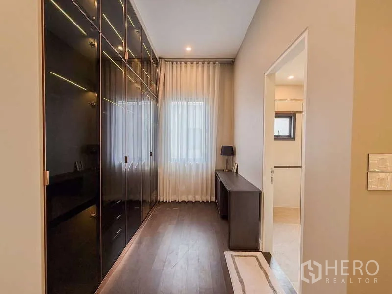 Detached House for rent or sale in Bang Kapi, Bangkok - Walk-in closet corridor with glossy floor-to-ceiling wardrobes and a small desk.