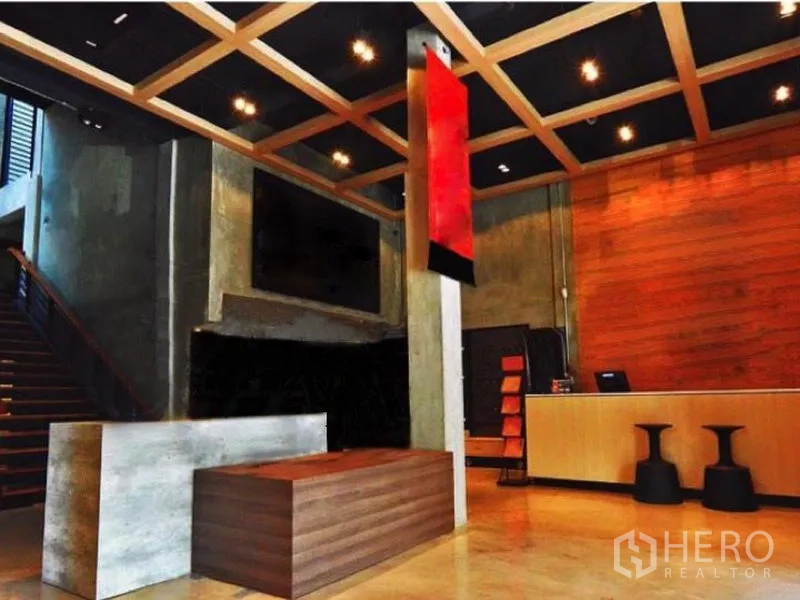 店屋 出租在Suan Luang, Bangkok - 商铺前台区，混凝土墙面与木格栅天花，红色吊牌、楼梯与长柜台，工业风十足。