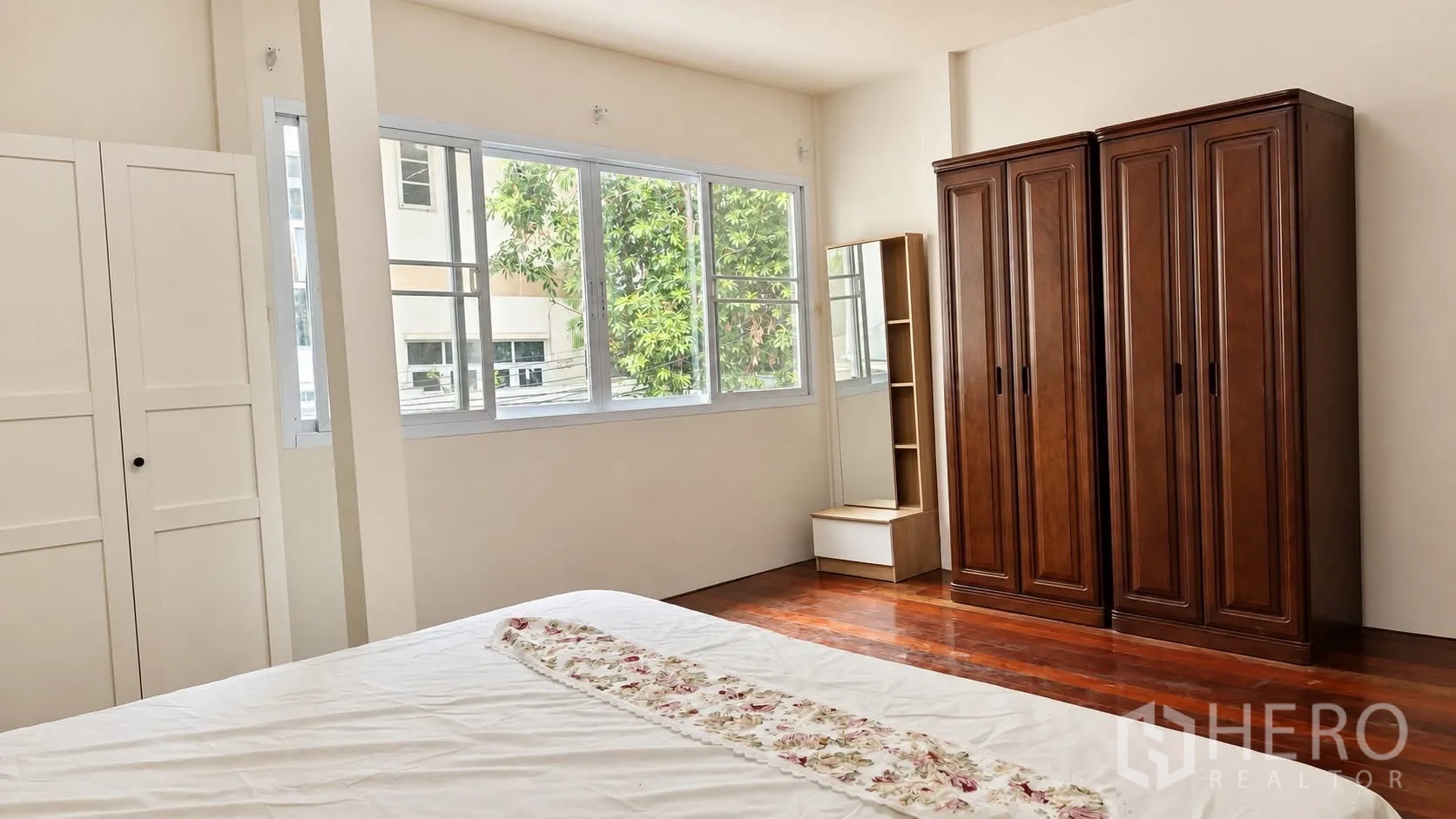 Detached House for rent in Khlong Toei, Bangkok - Bright bedroom with large windows, wooden floors, and wardrobes.