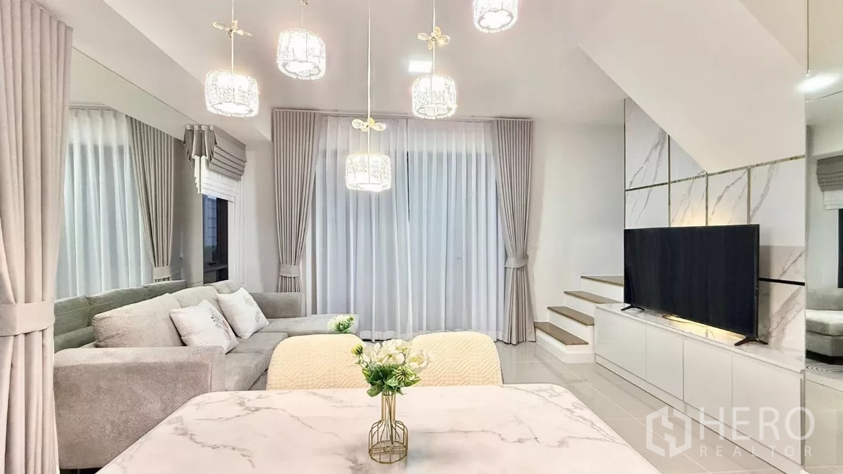 Townhouse for rent in Bang Phli, Samut Prakan - Bright lounge with L-shaped sofa, pendant lights and full-height curtains.