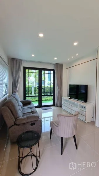 Detached House for rent in Samut Prakan - Cozy living room opening to the garden via black-framed glass doors.