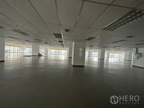 สำนักงาน ให้เช่า - พื้นที่สำนักงานเปิดโล่งกว้าง เพดานฝ้าทีบาร์ เสากลาง และกระจกบานกว้างมองเห็นวิวเมือง.