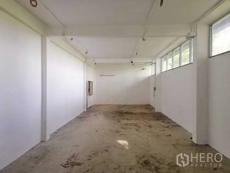Factory for rent in Pathum Thani - Clean white ancillary room with high windows and exposed lighting conduits over an unfinished floor.