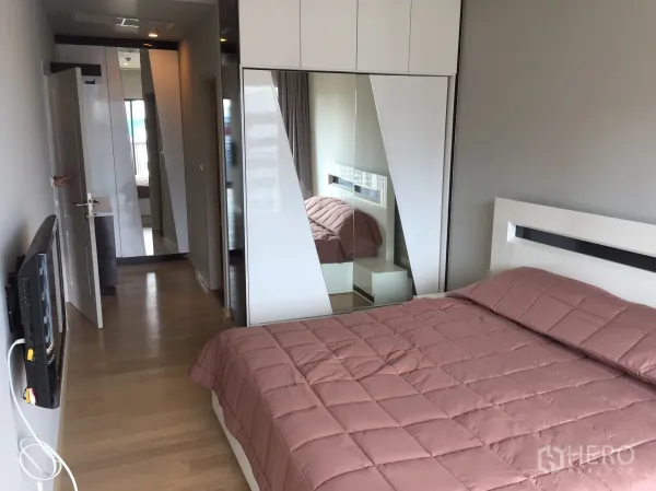 คอนโด ให้เช่าในBangkok - ห้องนอนพร้อมตู้เสื้อผ้าบิลท์อินบานกระจก ทีวีติดผนัง และพื้นไม้.