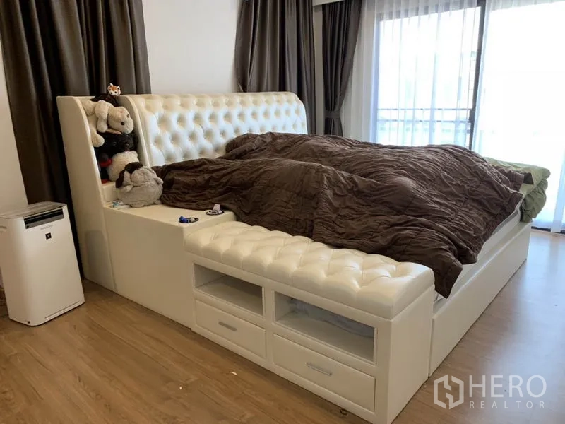 Detached House for rent or sale in Samut Prakan - Master bedroom with upholstered bed, wood flooring and sliding doors to balcony.