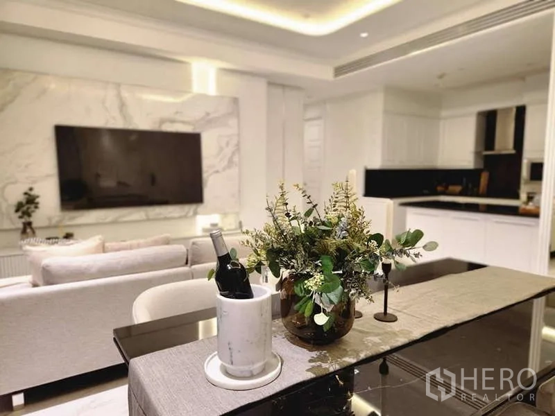 Condominium for sale in Watthana, Bangkok - Dining table view toward a marble TV feature wall and sleek white kitchen in a luxury Sukhumvit 31 condo.