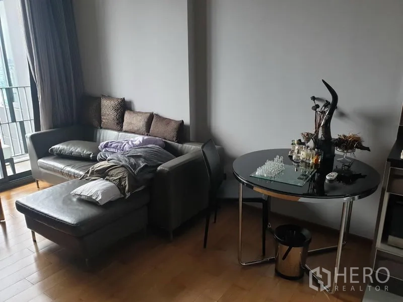 公寓 出租在Khlong Toei, Bangkok - 靠近阳台的舒适一角，灰色贵妃位沙发、圆形玻璃餐桌与木地板。