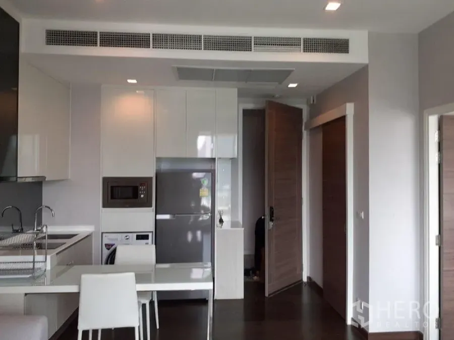 Condominium for rent in Ratchathewi, Bangkok - Open-plan kitchen and dining space with white table, cabinets and recessed lights.