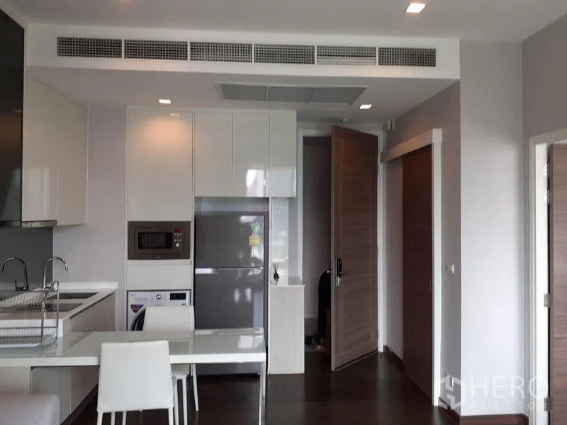 Condominium for rent in Ratchathewi, Bangkok - Open-plan kitchen and dining space with white table, cabinets and recessed lights.