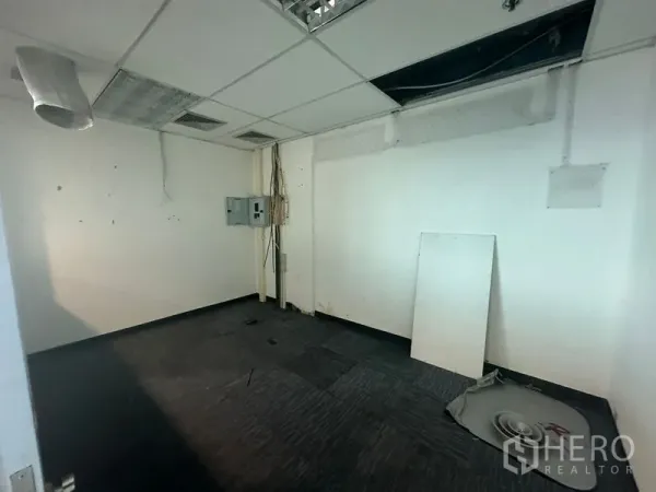 Office Space for rent in Watthana, Bangkok - Vacant utility room with exposed ceiling tiles, electrical panel, and dark carpet in Bangkok office.
