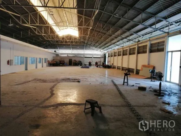 Factory for rent in Pathum Thani - Open warehouse floor under a gabled roof with skylight, machinery area and a glass side entrance.
