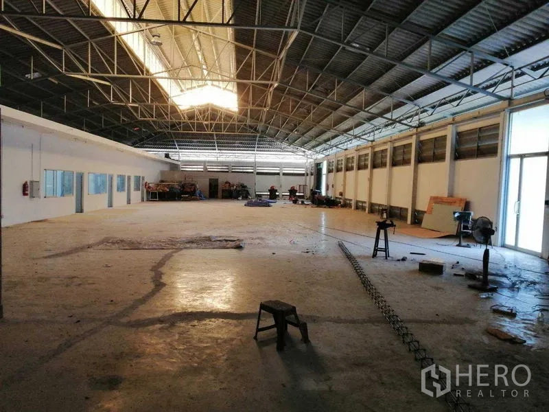 Factory for rent in Pathum Thani - Open warehouse floor under a gabled roof with skylight, machinery area and a glass side entrance.