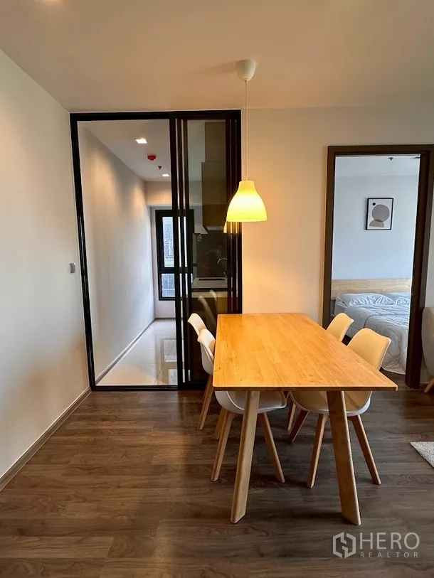 Condominium for rent in Chatuchak, Bangkok - Glass-partition kitchen seen from dining zone with wood flooring.