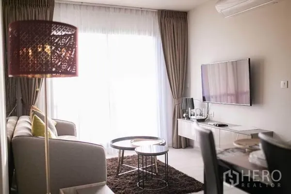 Condominium for rent in Pathum Wan, Bangkok - Living area with TV console, round nesting coffee tables and sheer curtains.