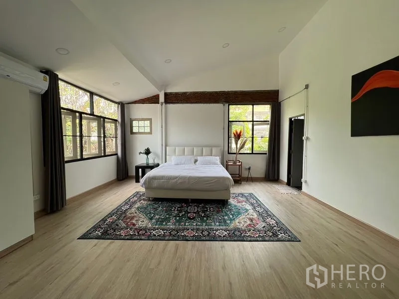 Townhouse for rent in Ratchathewi, Bangkok - Master bedroom view showing bed on an area rug and greenery through wide windows.
