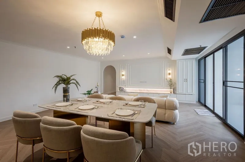 Condominium for sale in Watthana, Bangkok - Dining area set for six beneath a crystal chandelier beside floor-to-ceiling windows.