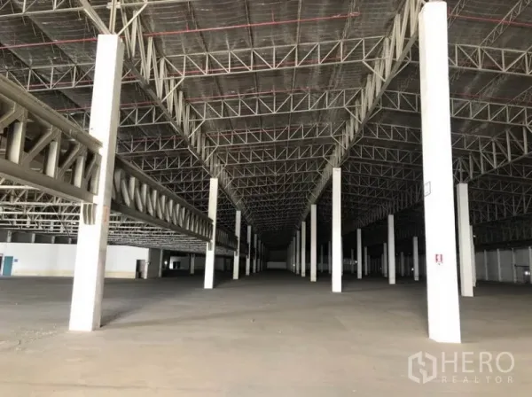 Warehouse for rent in Lam Luk Ka, Pathum Thani - Spacious warehouse interior with high steel truss roof, white columns, and open concrete floor.
