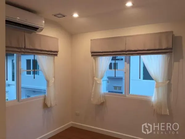 Townhouse for sale in Bang Khae, Bangkok - Corner bedroom featuring three windows, soft lighting and a wall AC unit.