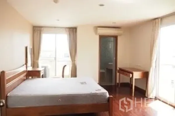 Condominium for rent in Pathum Wan, Bangkok - Master bedroom with wooden bed, desk, large windows and ensuite door.