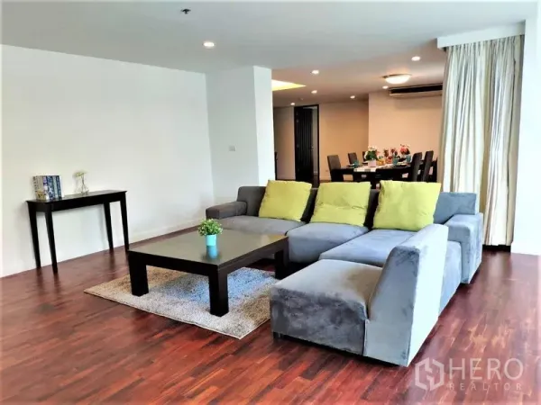 Condominium for rent in Bang Rak, Bangkok - Open-plan living and dining space with an L-shaped sofa and wood floors.