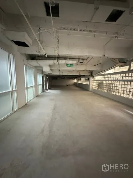 零售空间 出租 - 开放式零售室内，水泥地面、外露管线天花、磨砂玻璃窗与玻璃砖墙，并设紧急出口标识。