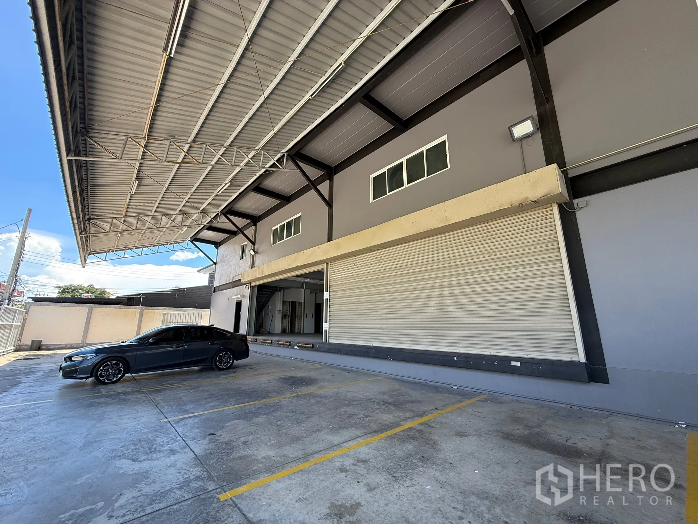 Warehouse for rent in Bueng Kum, Bangkok - Covered loading bay with roller shutter doors and marked parking in front of the warehouse.
