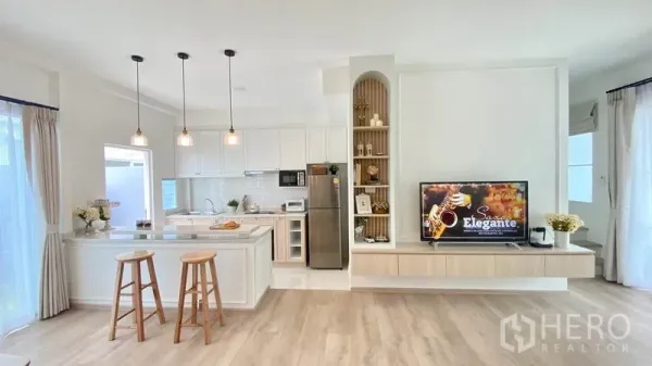 联排别墅 出租在Prawet, Bangkok - 白色厨房带中岛与吊灯，旁连客厅与电视柜