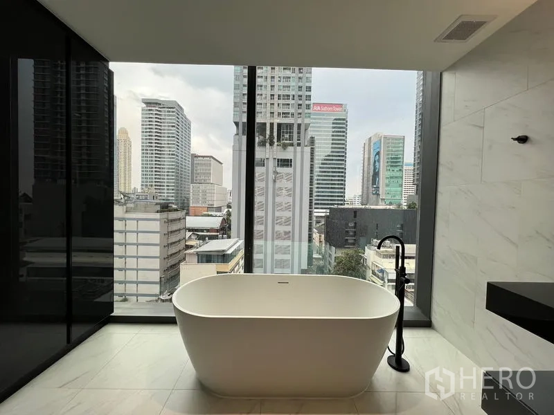 Condominium for rent in Bang Rak, Bangkok - Oval freestanding bathtub facing floor-to-ceiling window and skyline.