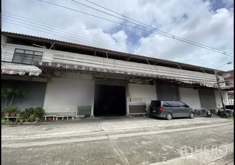 Warehouse for rent in Bang Khun Thian, Bangkok - Street-facing warehouse exterior in Bang Khun Thian with multiple roller shutters, covered loading bay, and parking area.