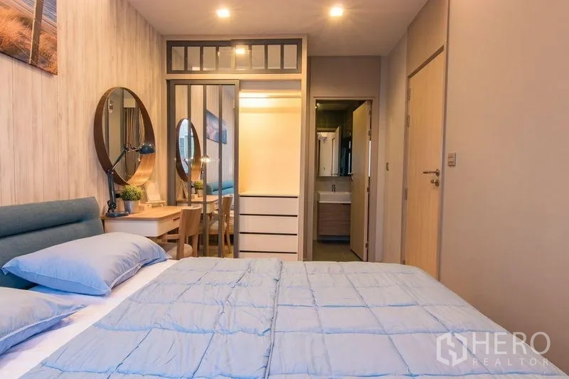 公寓 出售在Watthana, Bangkok - 卧室朝向镜面衣柜与书桌，旁有浴室门。