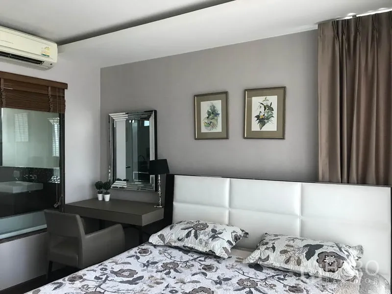 Condominium for rent in Watthana, Bangkok - Primary bedroom with upholstered headboard, desk and mirror, large window and neutral tones in a Watthana condo.