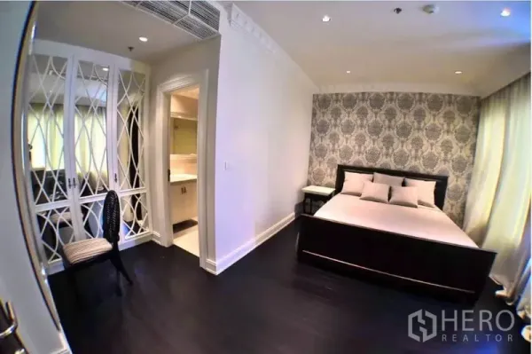 Condominium for rent or sale in Khlong Toei, Bangkok - Secondary bedroom with patterned accent wall, built-in wardrobes and work desk near en-suite.