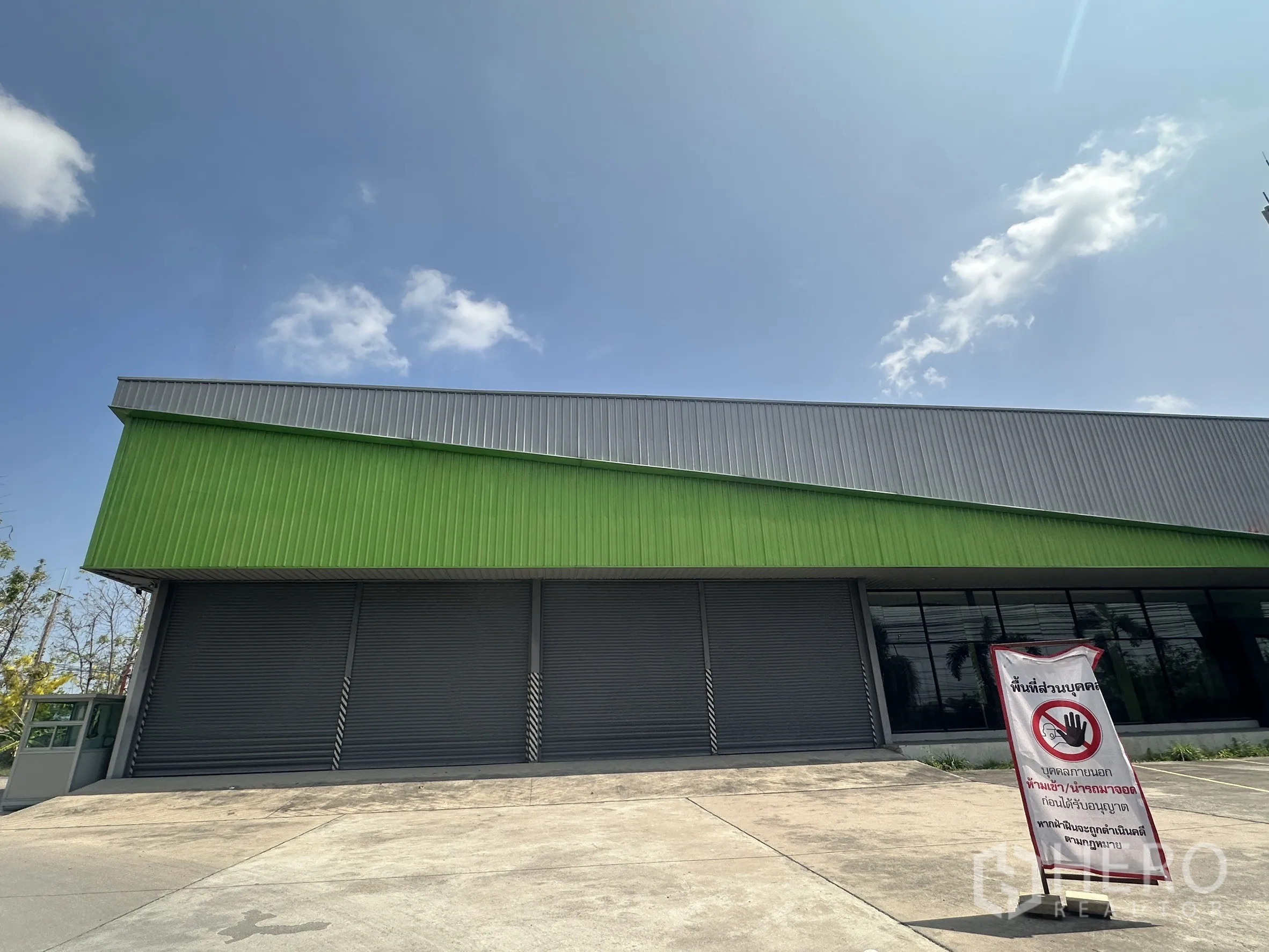 โชว์รูม for rent in Bang Pakong, Chachoengsao - ด้านหน้าอาคารโชว์รูมเมทัลชีทสมัยใหม่ มีประตูม้วนหลายบานและทางลาดโหลดสินค้า ใต้ท้องฟ้าโปร่ง