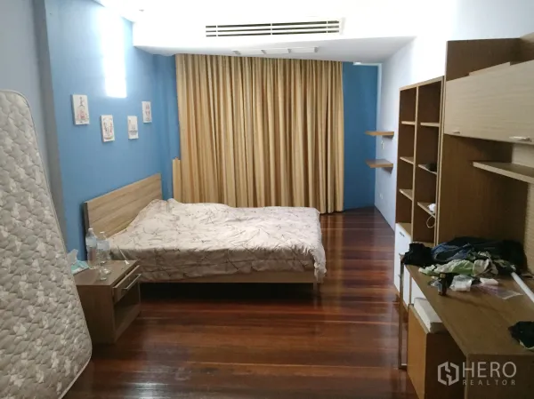 Townhouse for rent in Khlong Toei, Bangkok - Spacious bedroom with wooden flooring, blue accent walls, built‑in shelving and full curtains.
