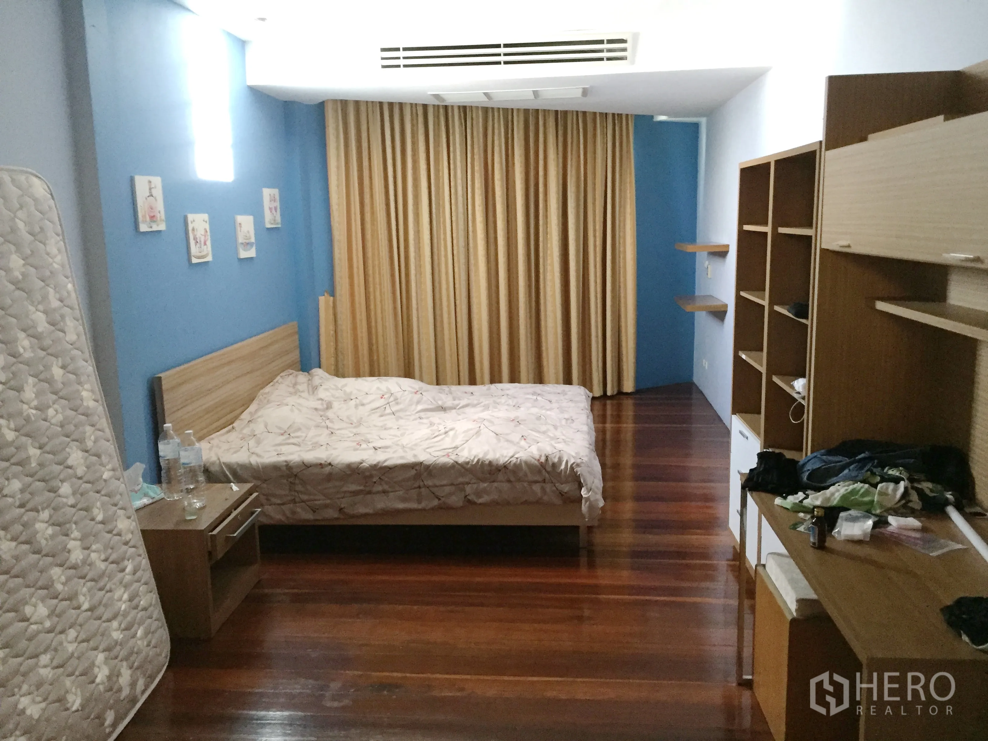 Townhouse for rent in Khlong Toei, Bangkok - Spacious bedroom with wooden flooring, blue accent walls, built‑in shelving and full curtains.