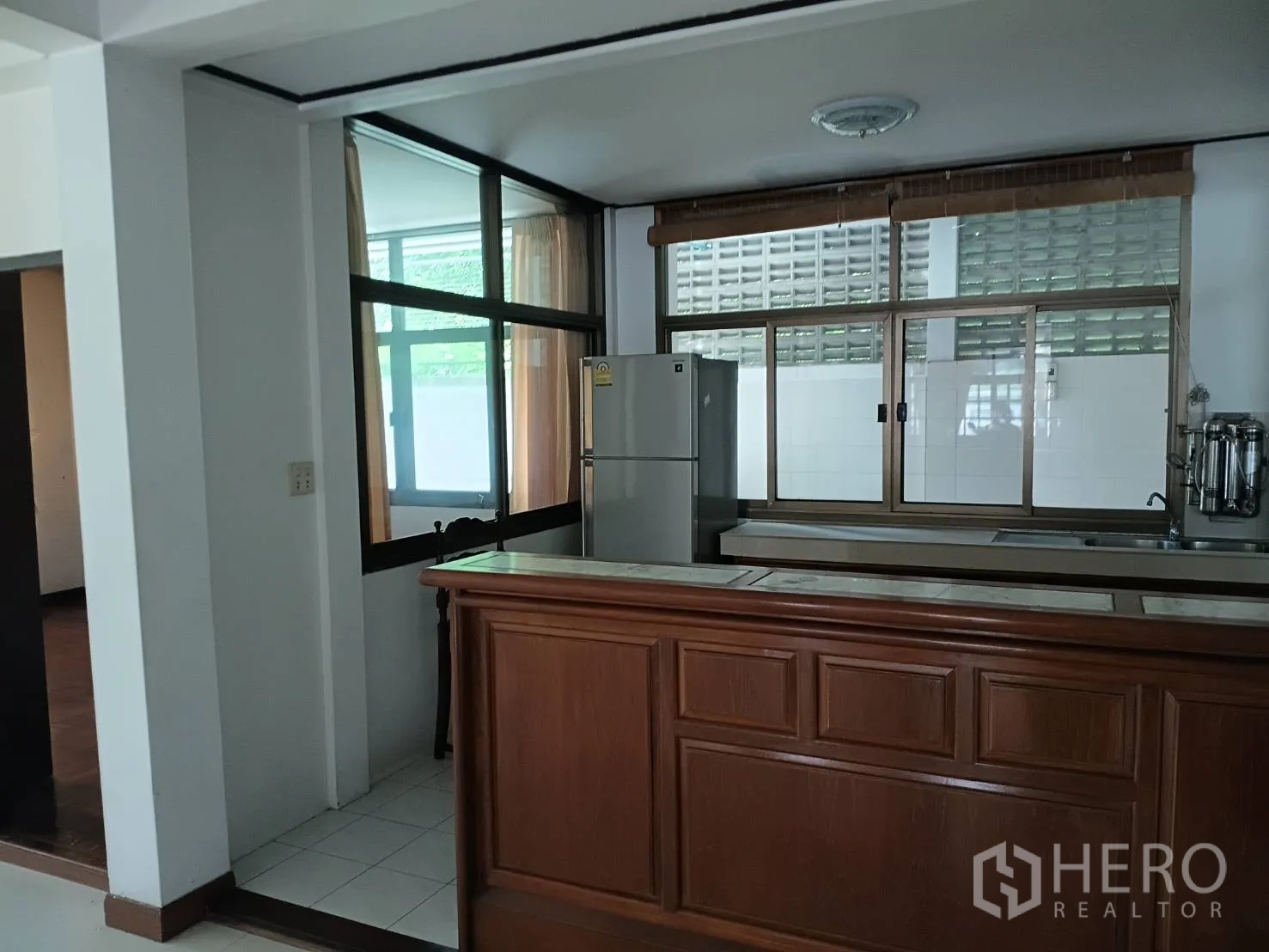 Detached House for sale in Watthana, Bangkok - Kitchen area with wooden bar counter, windows, and a refrigerator.