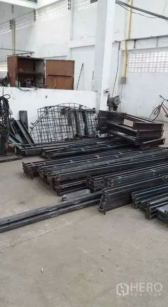 Warehouse for rent or sale in Nong Suea, Pathum Thani - Stacked steel beams and metal frames on a concrete floor inside a white warehouse.