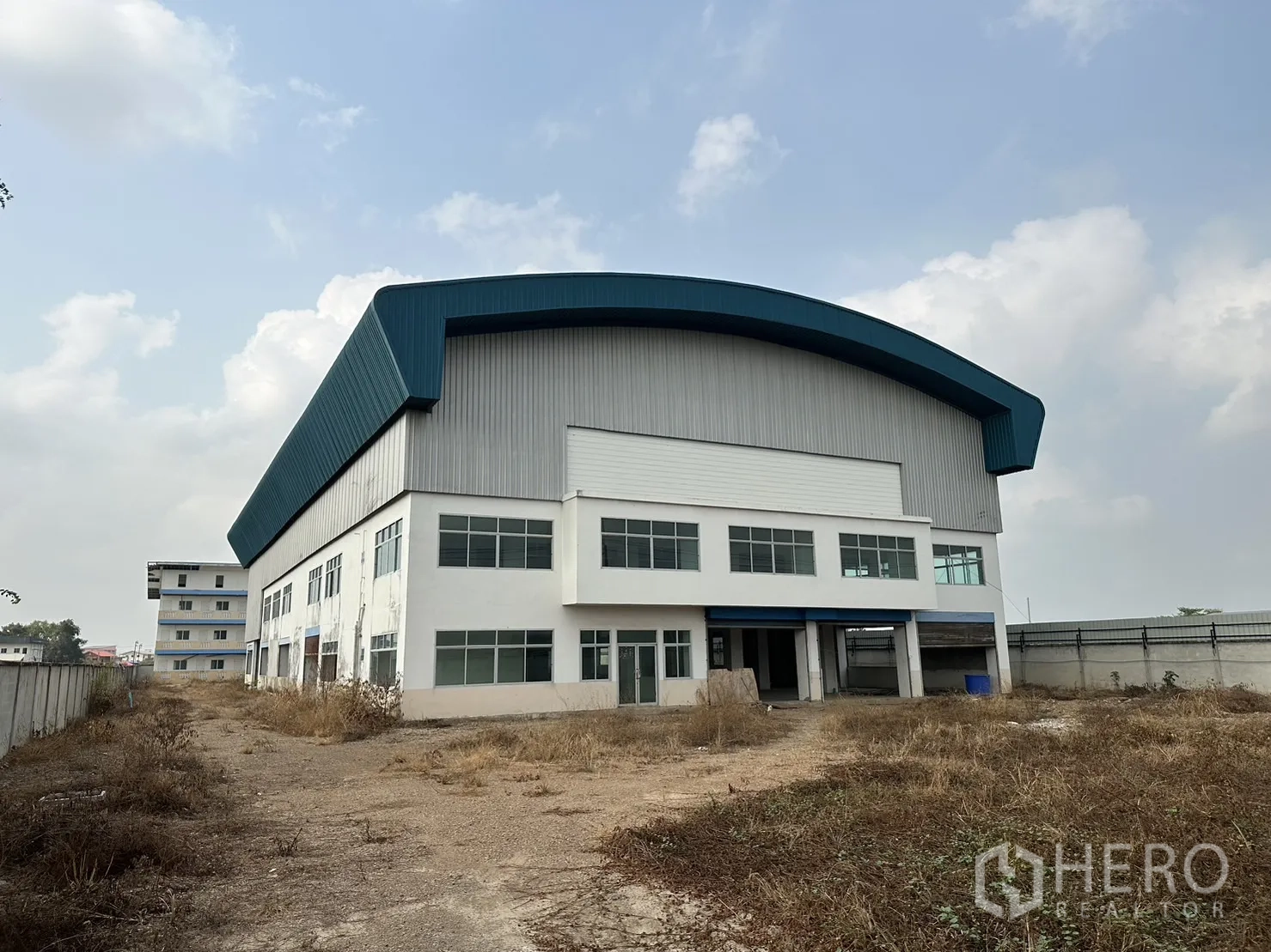 工厂 出租在Pak Kret, Nonthaburi - 大型工厂外立面，弧形蓝色屋顶和两层办公室窗户。